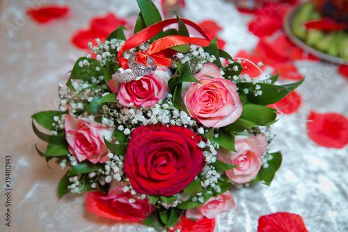 Rings on the wedding bouquet . The engagement rings are tied with ribbon Selective focus and blurred background . Gold wedding rings on a bouquet of red and white flowers.