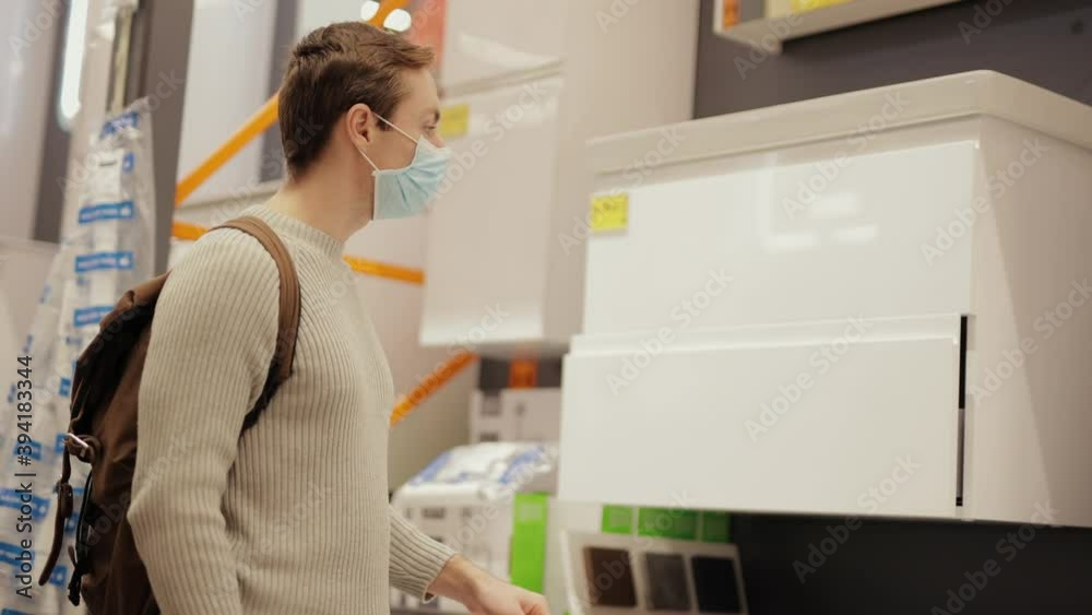 Man buyer chooses a shelves cupboard in the store with protective face mask