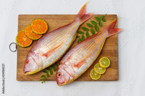 Top view of view of fresh Pink Perch (thread finned Bream) Decorated with lemon slice,Orange slice and curry leaves on a wooden pad,White Background,Selective focus. photo