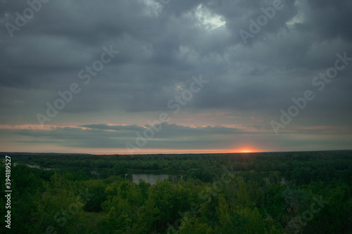The sun almost went down the horizon, cloudy gray blue sky, forest and river in the distance
