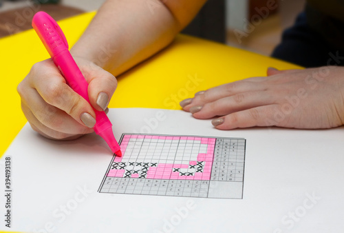 A woman is solving a Japanese crossword puzzle. Japanese crossword puzzle on yellow background