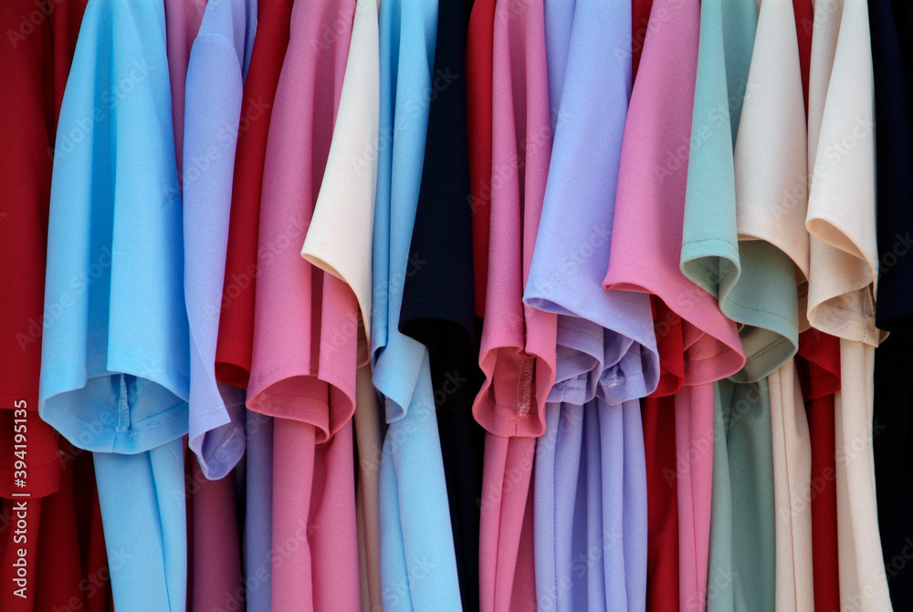 Pastel colour tee shirts hanging on a rail outside a shop.