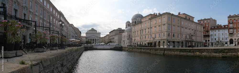 Panorama of Borgo Teresiano in Trieste, characterized by the Grand Canal, ancient buildings on both sides, and by the Church of San Paolo with neoclassical style positioned in front.