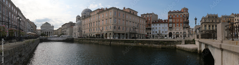 Panorama of Borgo Teresiano in Trieste, characterized by the Grand Canal, ancient buildings on both sides, and by the Church of San Paolo with neoclassical style positioned in front.