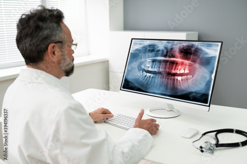 Mature Male Dentist Looking At Teeth X-ray On Computer