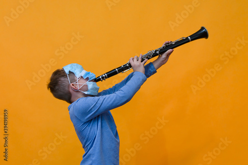 Photography A boy all in masks plays the clarinet, orange background.