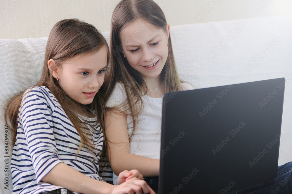 Two schoolgirls sitting at home on the couch emotionally looking at a laptop. Two schoolgirls sitting at home on the couch emotionally looking at a laptop.