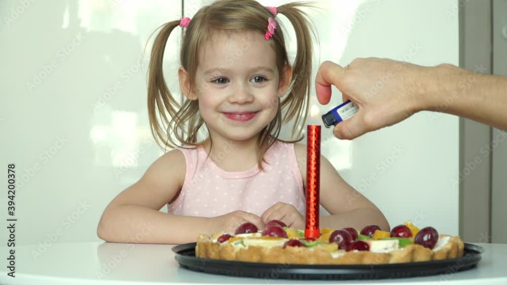 Little girl laughs, smiles and looks with delight at red burning fireworks in festive cake with fruits. Portrait of happy child celebrates birthday. Holiday concept Little girl laughs, smiles and looks with delight at red burning fireworks in festive cake with fruits. Portrait of happy child celebrates birthday. Holiday concept