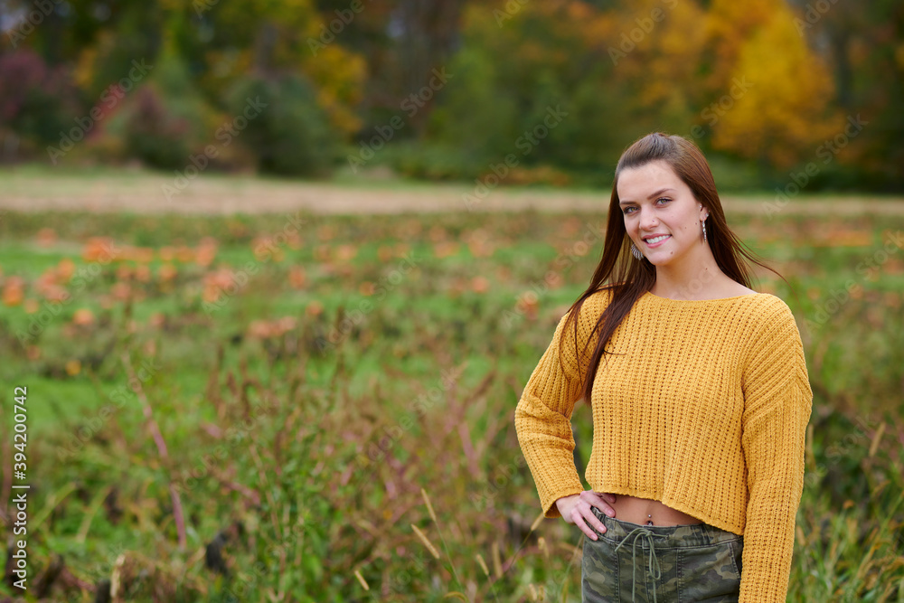 Adorable young woman in yellow crop sweater and camouflage pants stands in a pumpkin patch on farm - autumn holidays thanksgiving or Halloween themed Adorable young woman in yellow crop sweater and camouflage pants stands in a pumpkin patch on farm - autumn holidays thanksgiving or Halloween themed