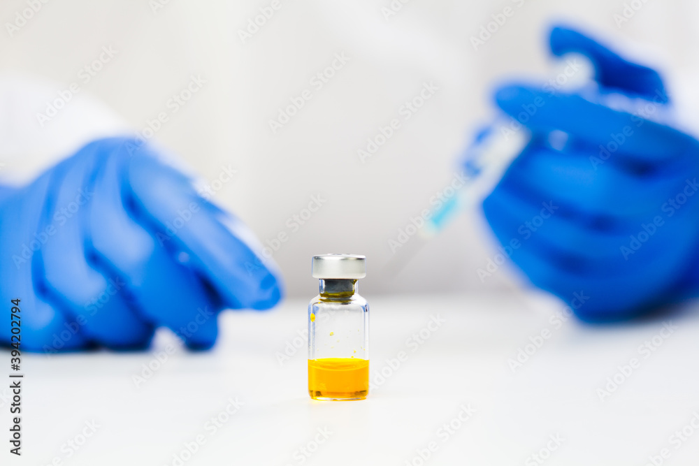 Yellow ampoule vaccine liquid vial on table,hands in blue protective medical gloves holding syringe jab,Coronavirus vaccine concept,cure treatment & therapy of COVID-19 infected patient,clinical trial Yellow ampoule vaccine liquid vial on table,hands in blue protective medical gloves holding syringe jab,Coronavirus vaccine concept,cure treatment & therapy of COVID-19 infected patient,clinical trial