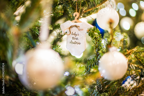 Baby's first Christmas porcelain and wood tree ornament decoration surrounded by lights and white and blue ornaments