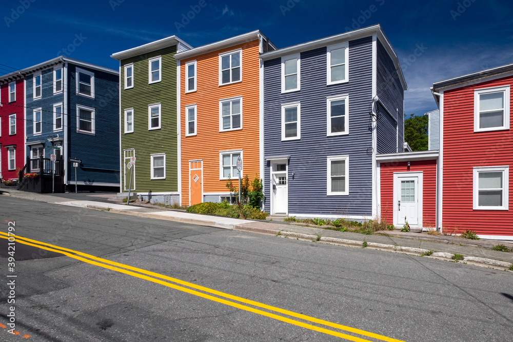 Street view of multiple colourful wooden buildings of various colours. The small structures have double hung windows and white doors. There's the blue sky in the background and the street in front. Street view of multiple colourful wooden buildings of various colours. The small structures have double hung windows and white doors. There's the blue sky in the background and the street in front.