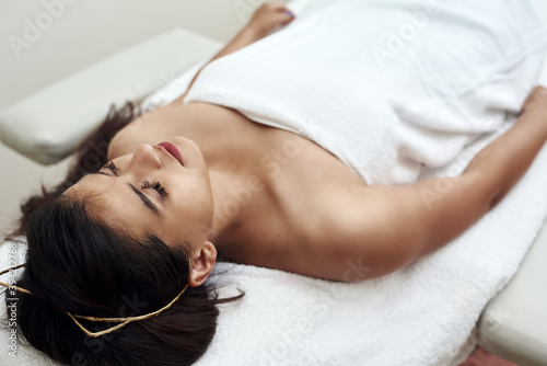 A young woman is lying on a couch by a beautician or masseur. Detached hair and bathrobe. Facial skin care. Woman in spa beauty salon