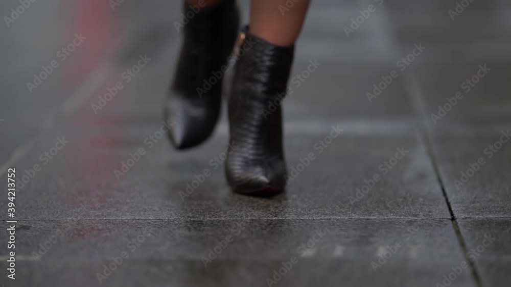 Women's feet in black shoes walk on a sidewalk made of tiles on a street in the city. Women's feet in black shoes walk on a sidewalk made of tiles on a street in the city.