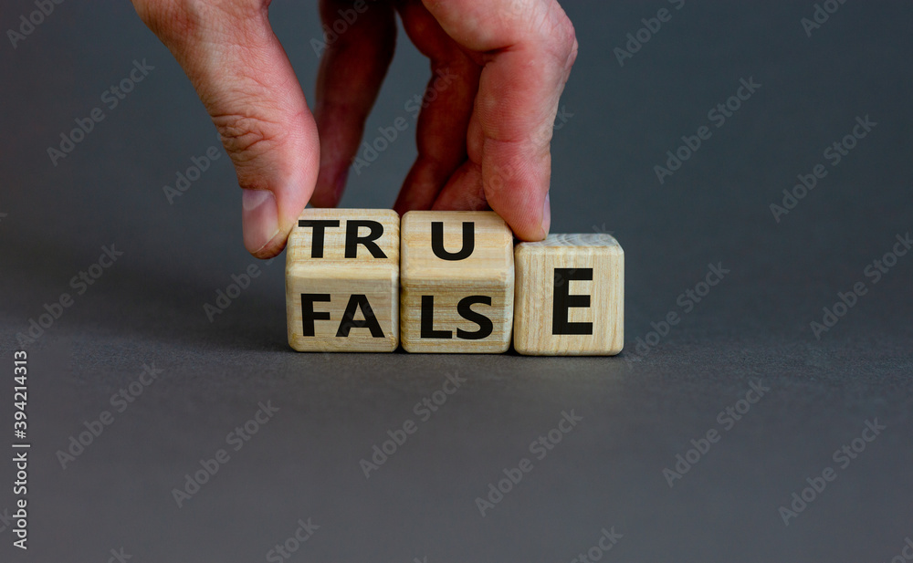 False or true. Male hand flips wooden cubes and changes the word 'false' to 'true' or vice versa. Beautiful grey background, copy space. Business and false or true concept. - obrazy, fototapety, plakaty 