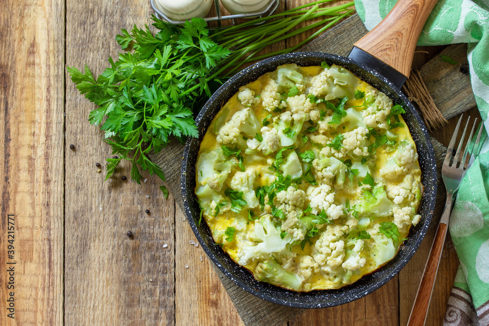 Diet breakfast or healthy lunch. Egg omelet with cauliflower in a cast-iron pan on rustic wooden table. Top view flat lay background. Copy space. Diet breakfast or healthy lunch. Egg omelet with cauliflower in a cast-iron pan on rustic wooden table. Top view flat lay background. Copy space.