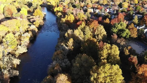 Flying over river and trees in fall color by residential neighborhood.