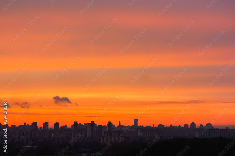 Silhouettes of houses against a bright orange sky at sunset or dawn. View of the horizon in the big city