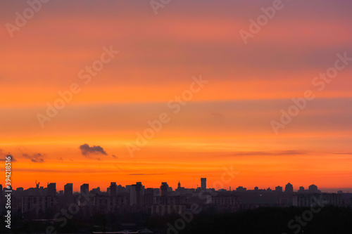 Silhouettes of houses against a bright orange sky at sunset or dawn. View of the horizon in the big city