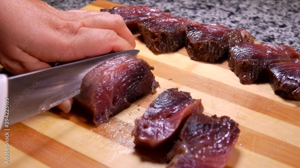 Female hands are slicing raw tuna fish onto pieces on a wooden board on the grey stone table Female hands are slicing raw tuna fish onto pieces on a wooden board on the grey stone table