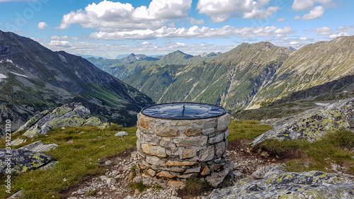 A pile of stones with a map on top of Arlh?he in Austrian Alps. The peak is surrounded by high Alps, stretching endlessly. There are a few clouds on the sky. Discovering and experiencing the nature photo