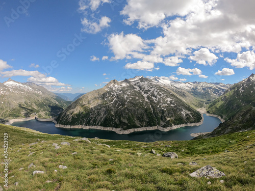 A panoramic view on an artificial, dam lake stretching over a vast territory around Alps in Austria. Lake is shining with navy blue color. In the back there are a few glaciers. Controlling the nature photo