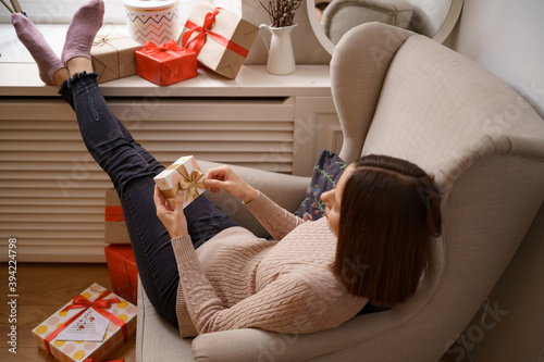 PRETTY young woman while sitting in a comfortable armchair holding a gift box surrounded by gifts at home. Ghe guesses what's inside © arthurhidden