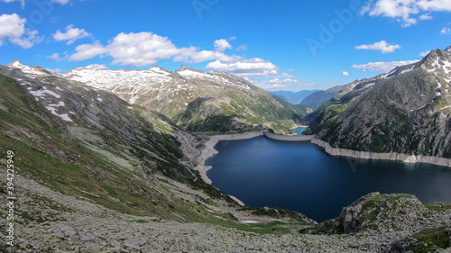 A panoramic view on an artificial, dam lake stretching over a vast territory around Alps in Austria. Lake is shining with navy blue color. In the back there are a few glaciers. Controlling the nature