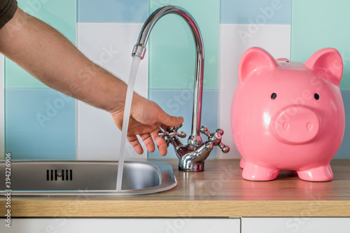 Fototapeta Naklejka Na Ścianę i Meble -  Flowing tap water and a piggy bank standing next to it. Water consumption price concept