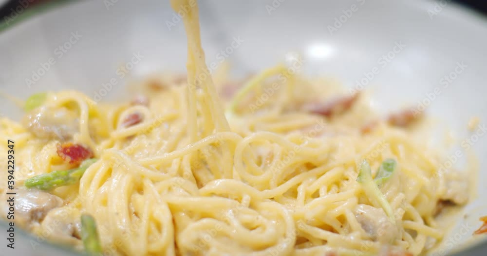 Close up fork rolling tasty delicious spaghetti carbonara with bacon in white plate at restaurant