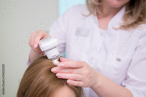 A trichologist examines the condition of the hair on the patient?s head with a dermatoscope