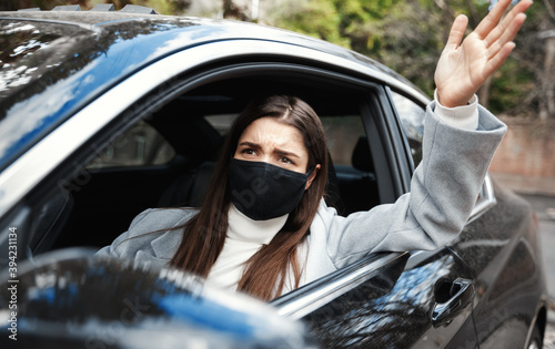 Annoyed woman in face mask scolding driver, sitting in car and looking out of window, arguing with person in car ahead. Businesswoman complaining on traffic