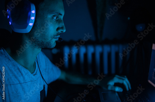 Un chico joven en una habitación oscura jugando al ordenador o trabajando como hacker con su portátil.