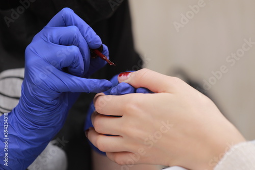 Master in protective gloves during a manicure at beauty salon. Master manicurist varnishes the marsala gel on the nails of a female client. The concept of beauty and health.