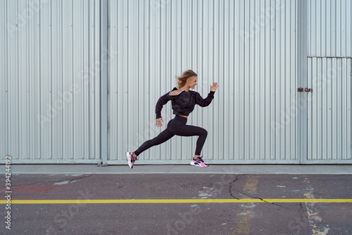 Modern young woman in sportswear jumping during outdoor workout on metalic background
