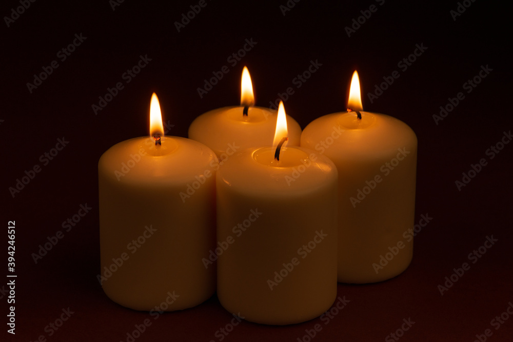 Four white candles flame burning on dark background with copy space for text.