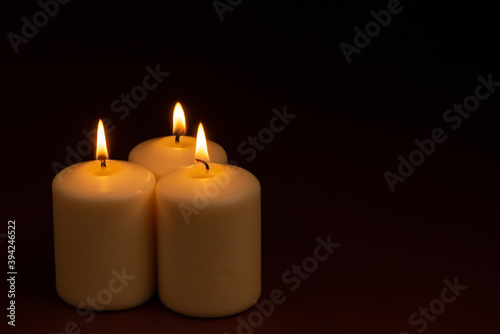 Three white candles flame burning on dark background with copy space for text.