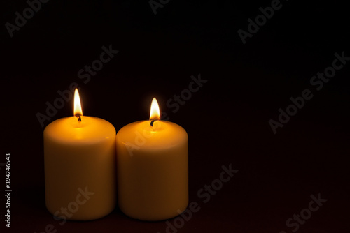 Two white candles flame burning on dark background with copy space for text.