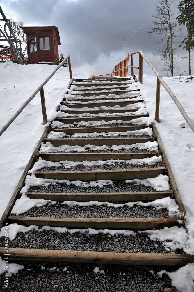 Obraz premium Wooden mountain trail in winter. Stairs with wooden railing in the mountains. Landscape with mountain path. Trail leading to the mountain peak. Adventure and travel.