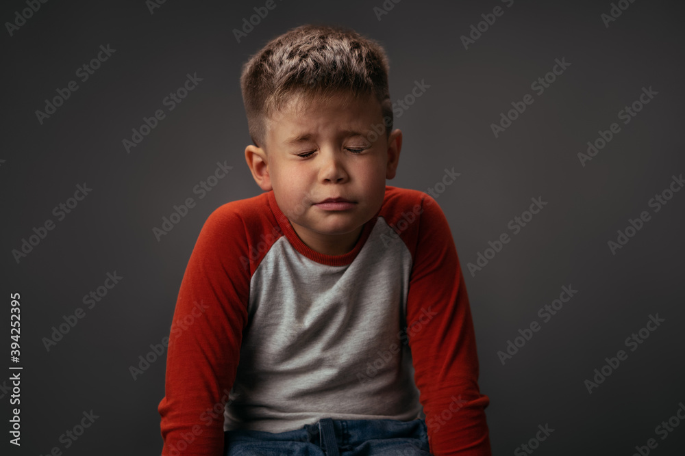 Making a wish little boy in red and white shirt sits on the chair with eyes shut. Making a wish for Christmas concept. Facial expressions, emotions, feelings.