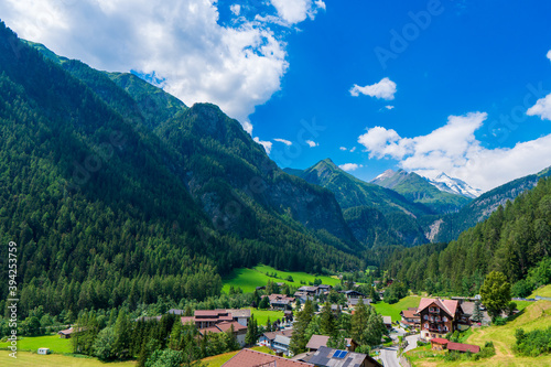 A scenic landscape photo of the Austrian municipality of Heiligenblut with St. Vincent Church in front of the Hohe Tauern mountains. Cetral Alps mountains in the background.