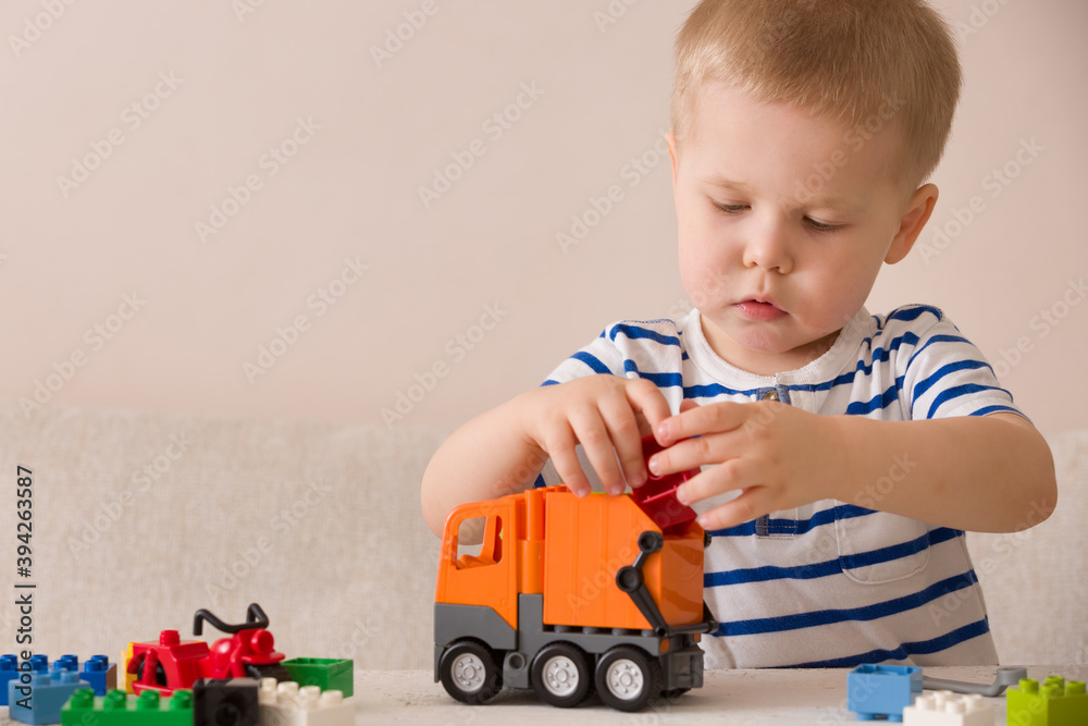 Toddler child is playing with a bright toy car and colorful cubes on the table. Multi-colored plastic cubes for early child development. Early learning and educational toys for a little boy Toddler child is playing with a bright toy car and colorful cubes on the table. Multi-colored plastic cubes for early child development. Early learning and educational toys for a little boy