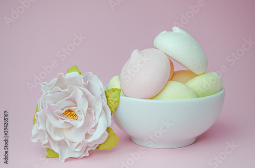 Meringues in a white Cup and a flower on a pink background.