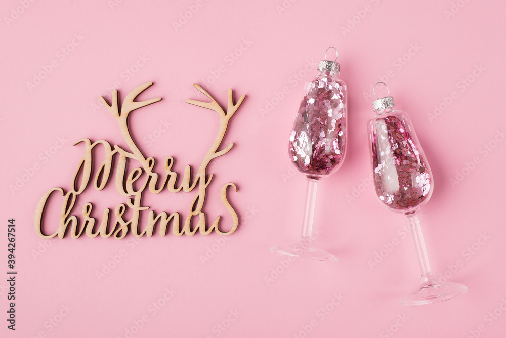 Christmas concept. Top above overhead view photo of wine glasses with pink confetti inside and wooden handmade merry christmas sign isolated on pastel pink background Christmas concept. Top above overhead view photo of wine glasses with pink confetti inside and wooden handmade merry christmas sign isolated on pastel pink background