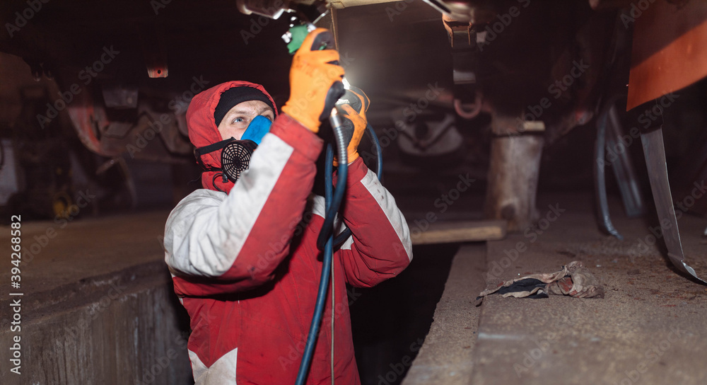 male worker in a respirator treats the underside of the car with anti-corrosion paint with a compressor.
