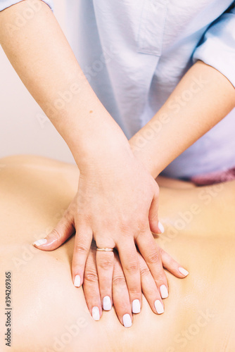 Massage therapist hands massaging client's back close-up in beauty salon