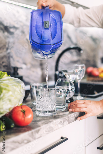 Woman pouring drinking water into a glass from a filter in the kitchen close-up, healthy eating, vertical photography