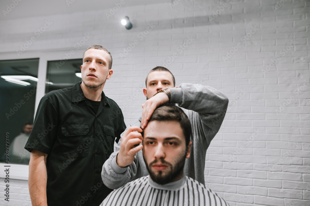 Φωτογραφία Two male hairdressers cut their bearded beautiful client's hair in a light barber shop