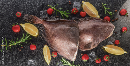 headless halibut with ice, lemon and tomatoes on black background