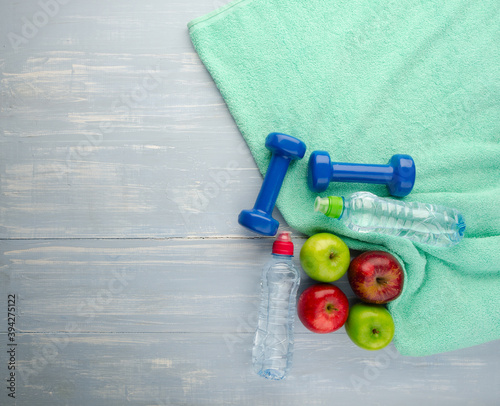 Colored Apples dumbbells sport water bottles and turquoise towel on blue wooden table background.